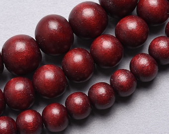 May include: Close-up of strands of round, dark red wooden beads. The beads are smooth and evenly sized, with a rich, warm color. The beads are strung together, suggesting they are for jewelry making or crafting.