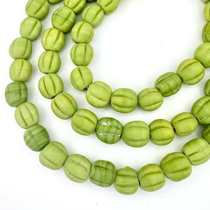 May include: Close-up of three strands of light green beads. Each bead has a rounded shape with vertical grooves, resembling small melons. The beads are strung together, creating a necklace or bracelet component. The background is plain white.