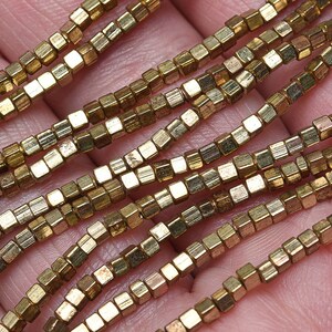 May include: A strand of gold-toned metal beads, each bead is a small cube with a slightly textured surface.