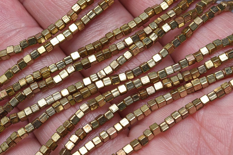May include: A strand of gold-toned metal beads, each bead is a small cube with a slightly textured surface.