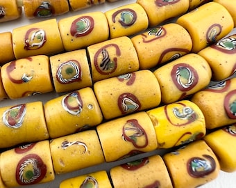 Pode incluir: Um fio de contas de vidro amarelo com manchas vermelhas, azuis e verdes. As contas são cilíndricas e têm uma superfície texturizada.