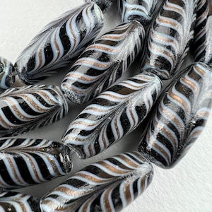 May include: A close-up of a strand of black and white glass beads with gold accents. The beads are oval shaped and have a swirling pattern.