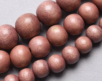 May include: Close-up of a strand of rose-gold wooden beads. The beads are round with a textured surface and are arranged in rows. The beads are approximately 1 inch in diameter.