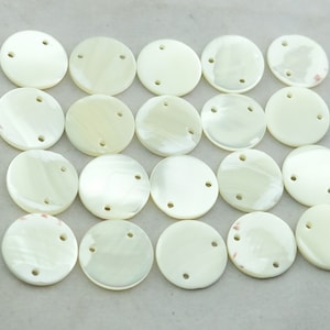 May include: Twenty white round shell buttons with two holes each. The buttons are arranged in a rectangular pattern.