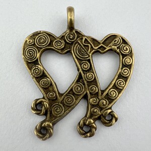 May include: A bronze-colored pendant featuring two intertwined hearts. Each heart is adorned with spiral designs and connected at the center and base. The pendant has a loop at the top for hanging.