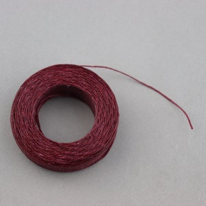 May include: A spool of maroon waxed thread with a long tail extending from the spool.