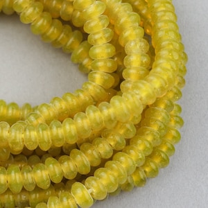 May include: A strand of yellow glass beads with a slightly frosted finish. The beads are small and round, and they are strung together on a clear thread.
