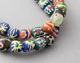 Pode incluir: Um fio de contas de vidro coloridas com vários padrões geométricos e florais. As contas são de forma oval e têm um acabamento brilhante.