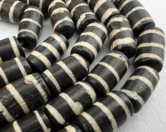 May include: Close-up of a collection of dark brown and white striped beads. The beads are cylindrical with white bands encircling the dark brown body. The beads are strung together, suggesting they are for jewelry making or crafts.