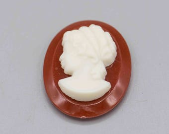 May include: A white cameo of a woman's profile in a red oval frame.