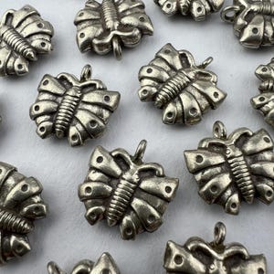 May include: A collection of silver-toned butterfly charms with intricate details. Each charm features a raised butterfly design with a textured body and wings.