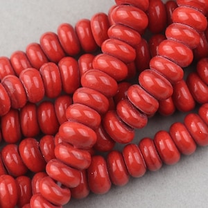 May include: A strand of bright red, glossy, ceramic beads. Each bead is a small, rounded cylinder with a hole in the center. The beads are stacked on top of each other, creating a spiral pattern.