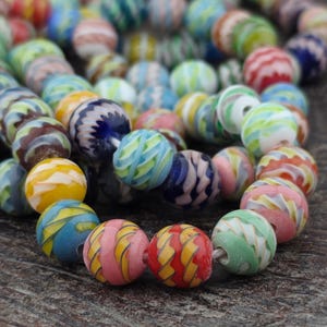 May include: A strand of colorful glass beads in various sizes and patterns. The beads feature swirls of yellow, blue, pink, green, and red. The beads are strung together on a white string, perfect for jewelry making or crafting.