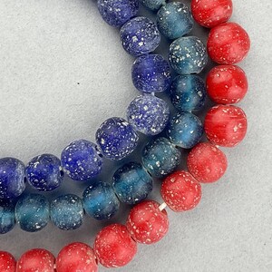 Peut inclure: Un collier de perles de verre bleues et rouges avec un motif moucheté. Les perles sont enfilées sur un cordon blanc.