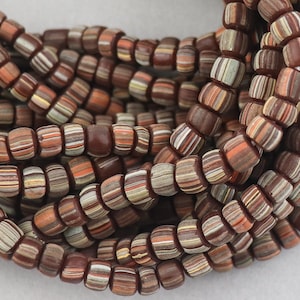 May include: A close-up of a strand of brown, white and orange striped glass beads. The beads are small and round, and they are arranged in a random pattern.