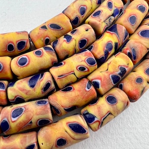 May include: A close-up of a string of yellow, orange, and blue glass beads. The beads are cylindrical and have a mottled pattern.