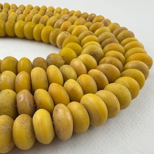 May include: A necklace of yellow beads, oval-shaped with a textured surface and varying shades of yellow and brown. The beads are arranged in a curved pattern. The necklace is shown in close-up.