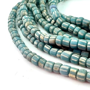 May include: Strands of blue and white striped beads. The beads are cylindrical with a slightly rounded shape. The color is a light blue with white stripes. The beads are strung together, creating a necklace or bracelet.