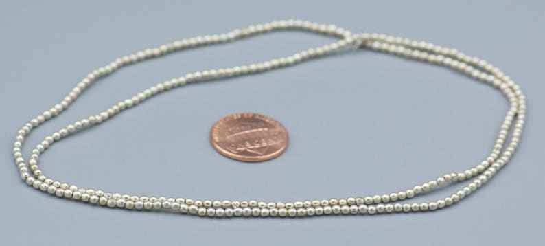 以下が含まれることがあります： 小さな丸いビーズで作られたシルバーネックレス。ネックレスは日本の1円玉と同じくらいの大きさです。