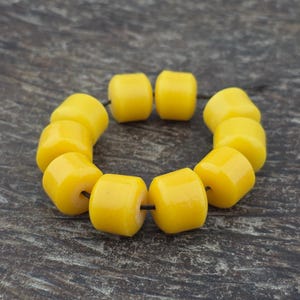 May include: A circular arrangement of nine smooth, cylindrical yellow beads strung on a thin black cord. Each bead features a glossy finish and a central hole, creating a uniform, bright yellow color profile across the entire set of jewelry components.