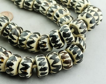 May include: A strand of white and black patterned beads. The beads are round and have a slightly irregular shape. The pattern on the beads is a series of black lines that create a geometric design.