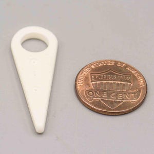 May include: A white plastic tool with a pointed tip and a small hole in the center. The tool is shaped like a triangle with a rounded top. A copper penny is in the background.