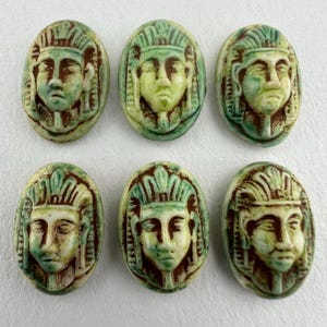May include: Six oval-shaped green and brown ceramic buttons with raised images of pharaohs' faces.