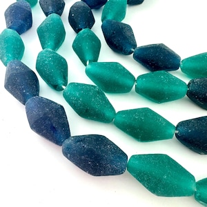 May include: Close-up of sea glass beads in teal and blue hues. The beads have a faceted shape and a textured surface. The beads are strung together, ideal for jewellery making or other craft projects.