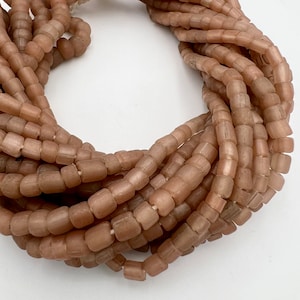 May include: A strand of light brown glass beads, each bead is square shaped with rounded edges.