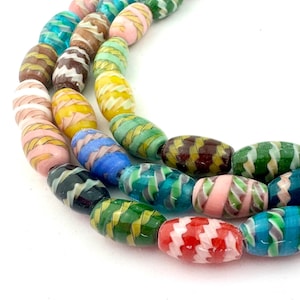 Peut inclure: Gros plan sur un fil de perles de verre colorées. Les perles sont de forme ovale avec un motif rayé dans diverses couleurs, dont le rose, le jaune, le vert, le bleu et le marron. Les perles sont enfilées, créant un motif vibrant et accrocheur.