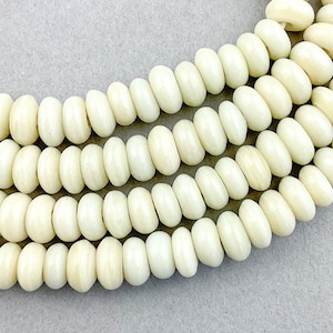 Puede incluir: Una hebra de cuentas redondas de color blanco hueso hechas de hueso. Las cuentas son lisas y tienen un acabado ligeramente brillante.