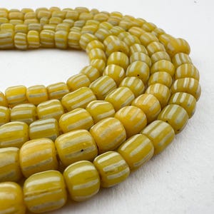May include: A strand of yellow glass beads with white stripes. The beads are cylindrical and have a slightly irregular shape.