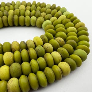 May include: A strand of green glass beads, each bead is smooth and slightly rounded. The beads are arranged in a circular pattern, creating a decorative and eye-catching display.