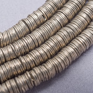 May include: A close-up of a silver necklace made of stacked, round, flat beads. The beads are arranged in rows and have a textured surface.