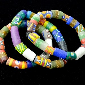 May include: A set of four colorful glass bead bracelets. The beads are cylindrical and have various patterns and colors, including green, blue, red, yellow, white, and purple.