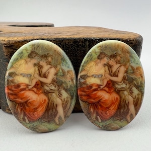 May include: A pair of oval-shaped ceramic earrings with a vintage-inspired design. The earrings feature a scene of two women in a garden setting, with a red, orange, and green color scheme.