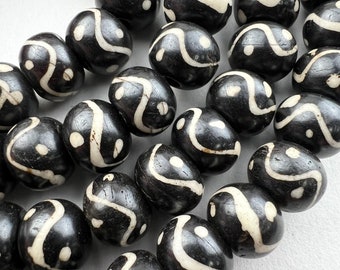May include: Close-up of a collection of dark brown beads with a white, wave-like pattern. The beads are oval-shaped and appear to be strung together. The beads have a glossy finish and a unique design.