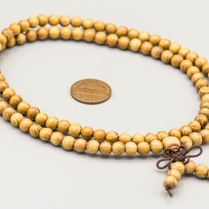 May include: A long strand of wooden beads in a light brown color. The beads are strung together with a brown cord and have a tassel at the end.