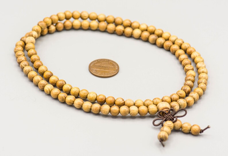 May include: A long strand of wooden beads in a light brown color. The beads are strung together with a brown cord and have a tassel at the end.