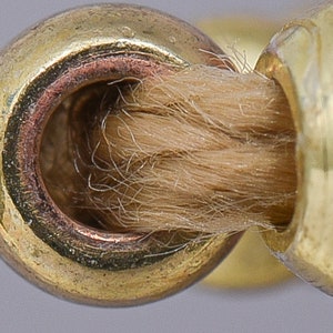 Pode incluir: Close-up de um aparador de pavio de metal dourado com um pavio castanho no interior.
