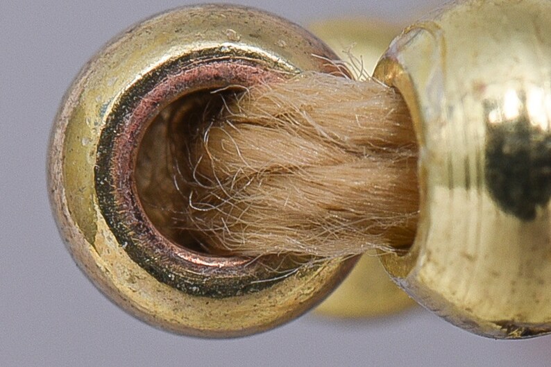 Pode incluir: Close-up de um aparador de pavio de metal dourado com um pavio castanho no interior.