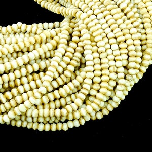May include: A strand of off-white, round, wooden beads. The beads are small and have a slightly irregular shape.