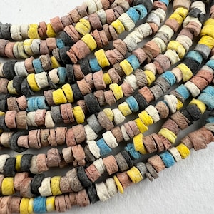 May include: A strand of colourful, round, ceramic beads. The beads are a mix of brown, white, yellow, blue, and black. The beads are all different sizes and shapes.