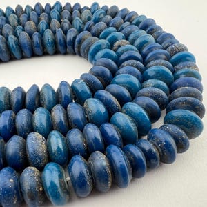 May include: A strand of blue glass beads with a speckled gold finish. The beads are round and have a slightly flattened shape.