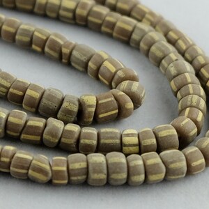 May include: A strand of brown and beige glass beads with a striped pattern. The beads are small and round, and they are strung together on a clear thread.