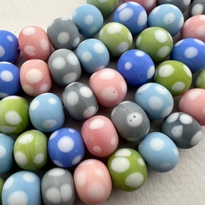 May include: A collection of colorful glass beads with white polka dots. The beads are in shades of blue, green, pink, and gray.