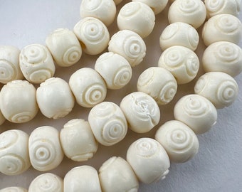 May include: A strand of white bone beads with a carved circular pattern. The beads are round and smooth, and they are strung together on a white cord.