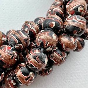 May include: A close-up of a strand of black, white, and red glass beads with gold accents. The beads are round and have a marbled pattern.