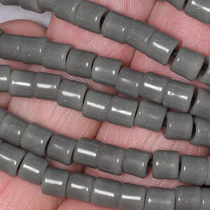 May include: A strand of gray ceramic beads, each bead is cylindrical in shape with a slightly textured surface.
