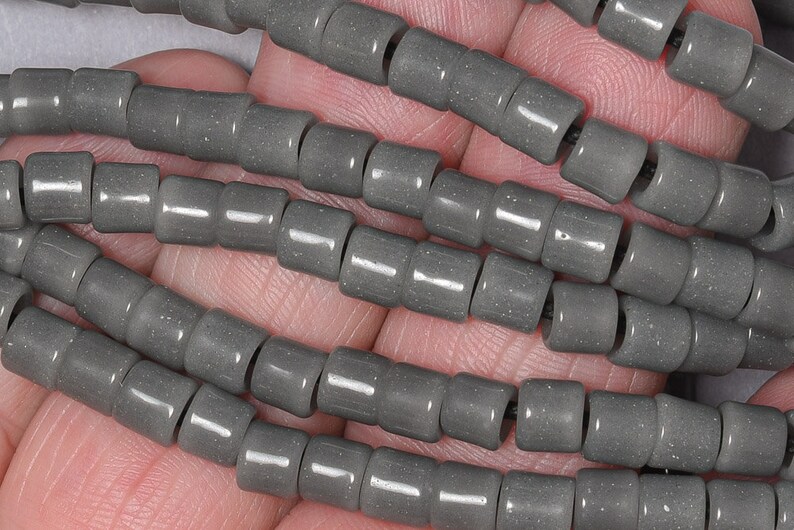 May include: A strand of gray ceramic beads, each bead is cylindrical in shape with a slightly textured surface.